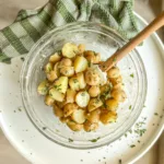 Potato salad in bowl seasoned with herbs and served with wooden spoon