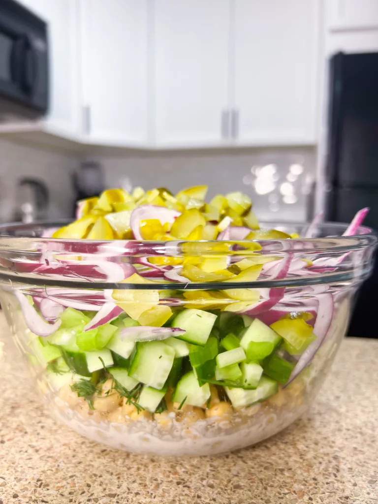 salad ingredients in bowl dressing, chickpeas, cucumber, red onion, yellow pepper