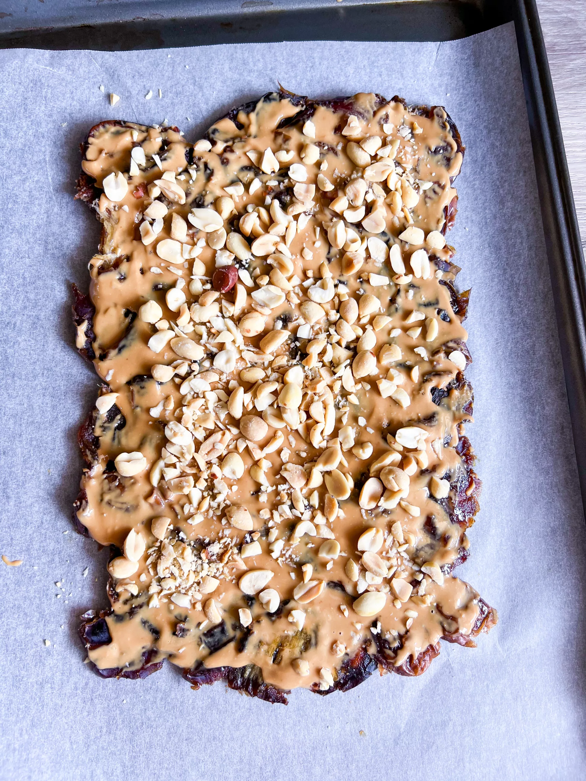 dates flattened on baking sheet with peanut butter and peanut pieces