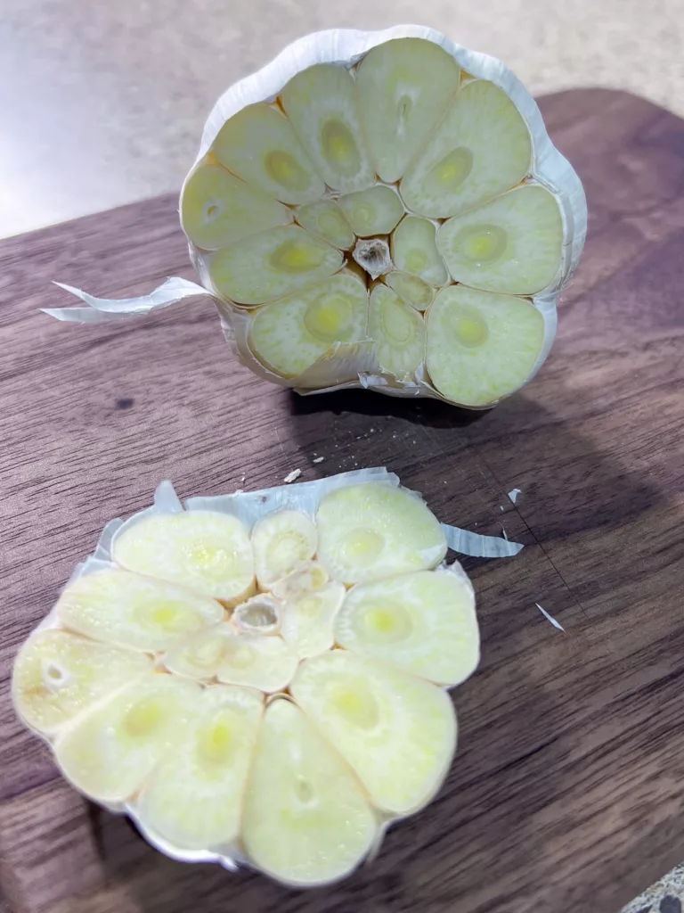 garlic cut in half on wood cutting board