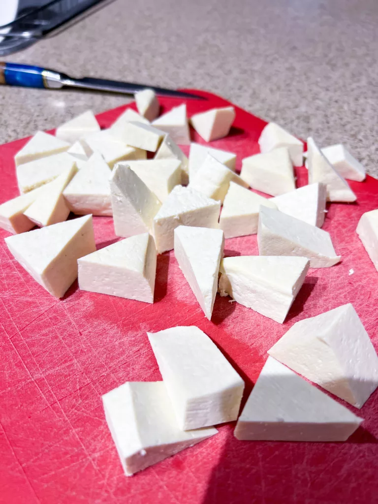 Tofu cut into triangles on red cutting board