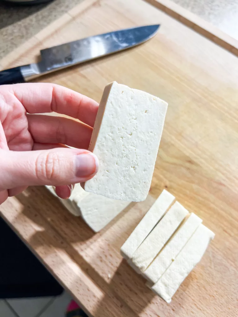 tofu on wood cutting board with hand