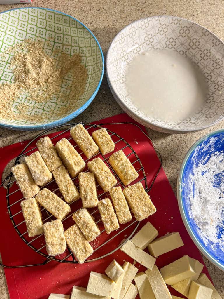 A cooling rack with a bunch of tofu breaded sticks on it.