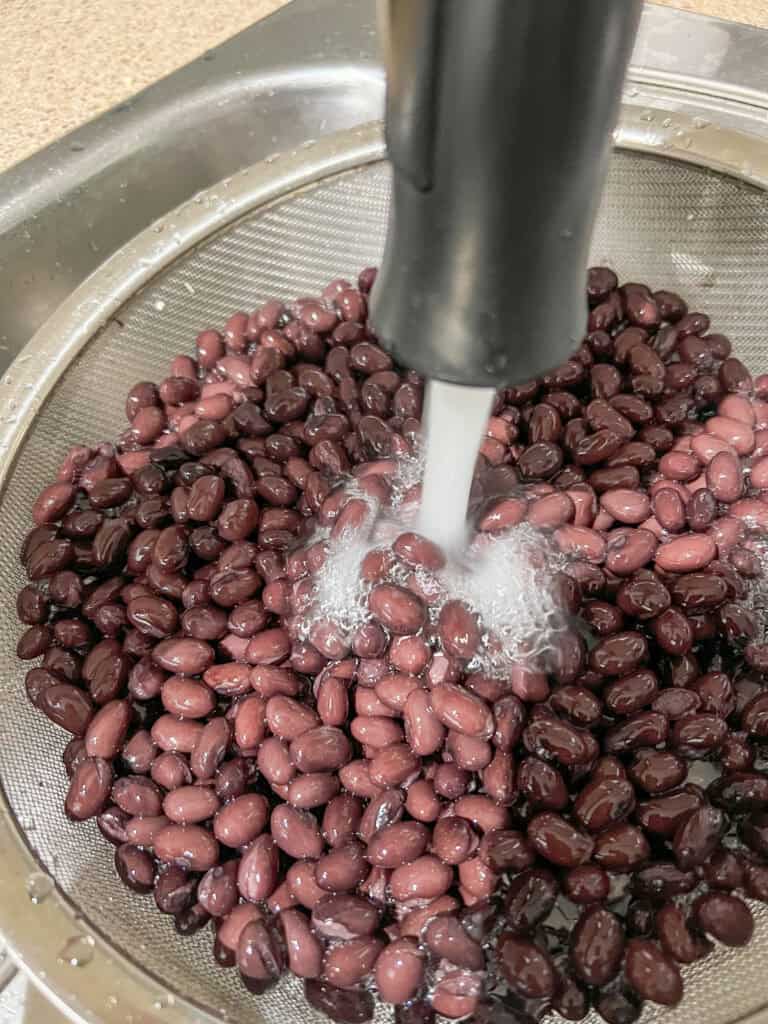 rinsing black beans in a stainer under sink