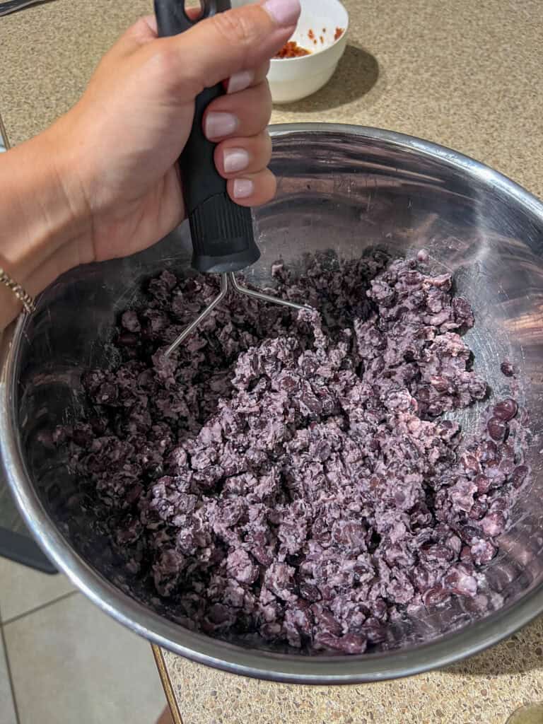 black beans mashed up in stainless steel mixing bowl