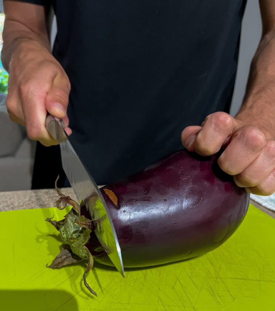 cutting the ends off a eggplant on a green cutting board