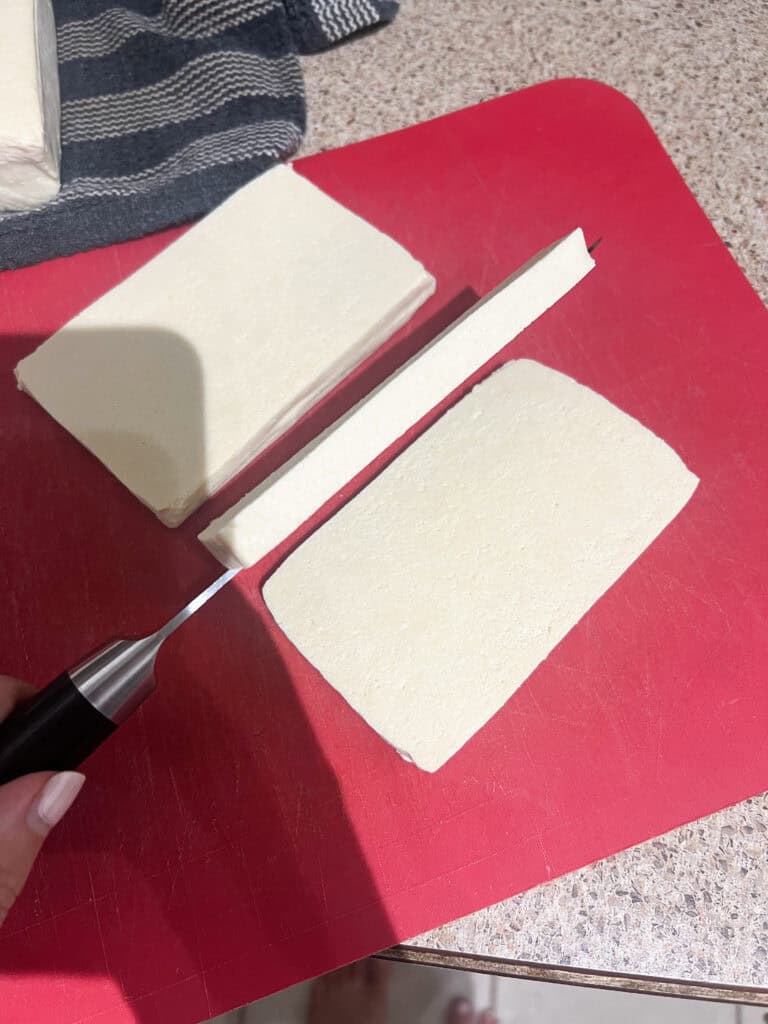 cutting the tofu into slices on red cutting board