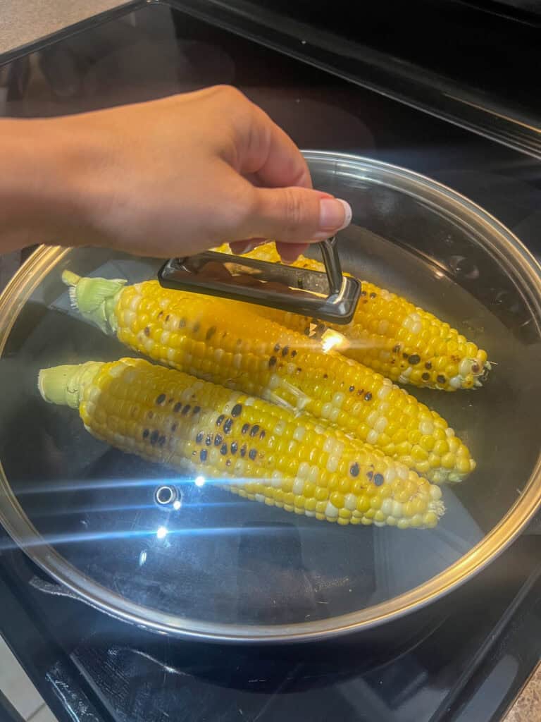 hand on lid steam corn in cast iron