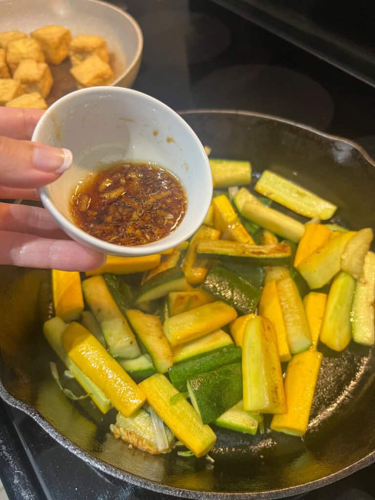adding the Hibachi sauce to the Zucchini on cast iron pan with onions