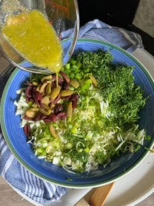 greek dressing being poured on cabbage salad