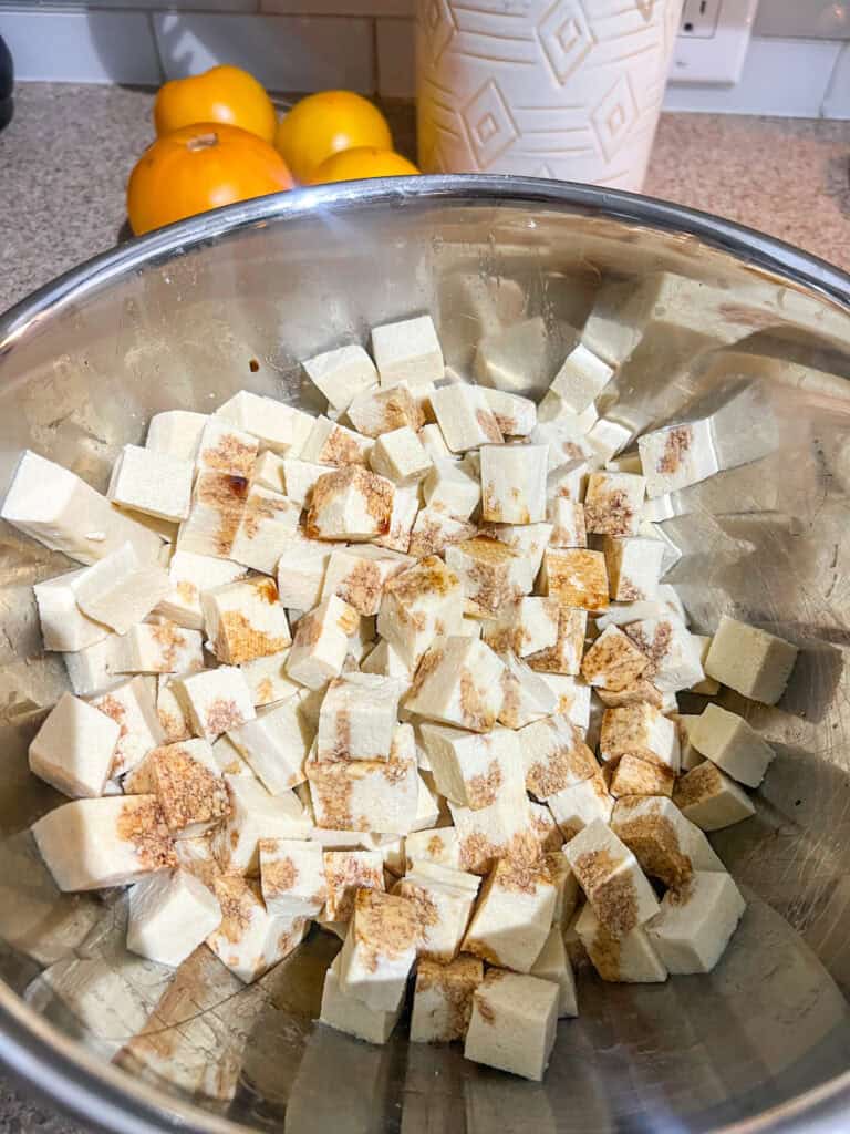 uncooked tofu with spices in silver mixing bowl