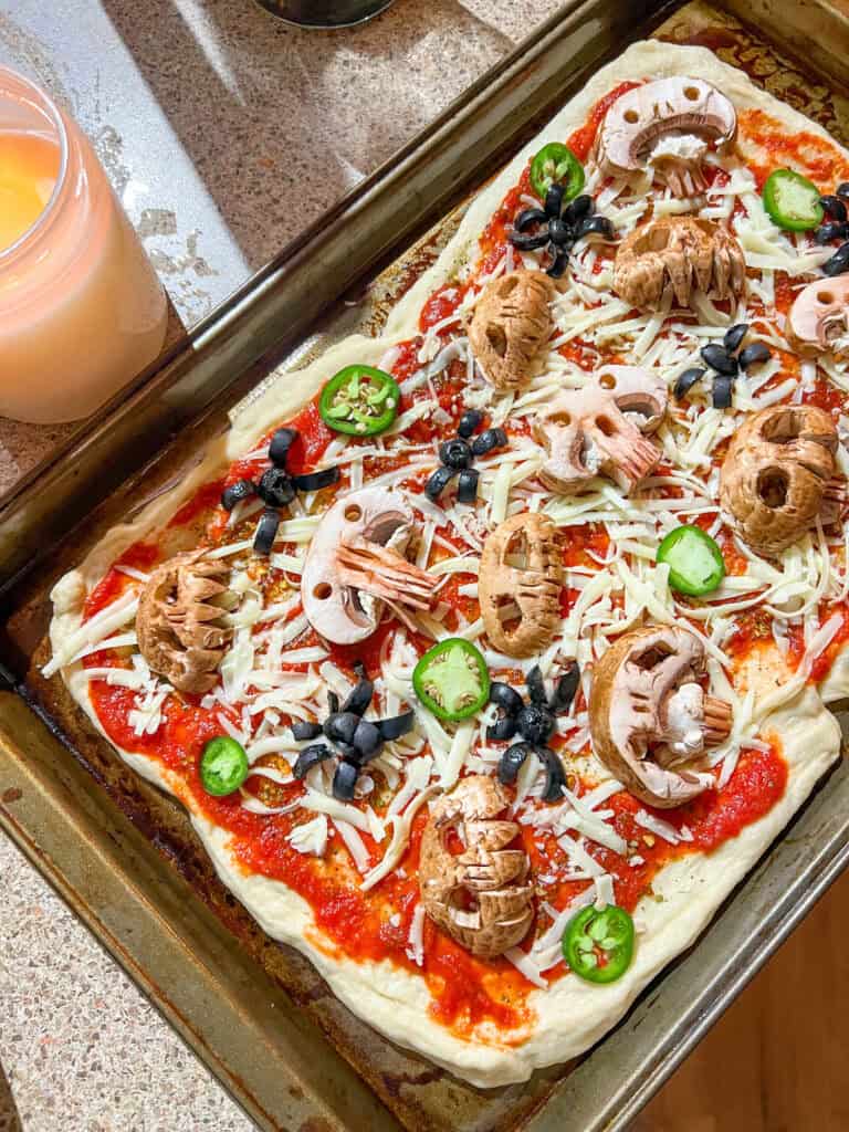 uncooked halloween pizza with skull mushrooms and olive spiders