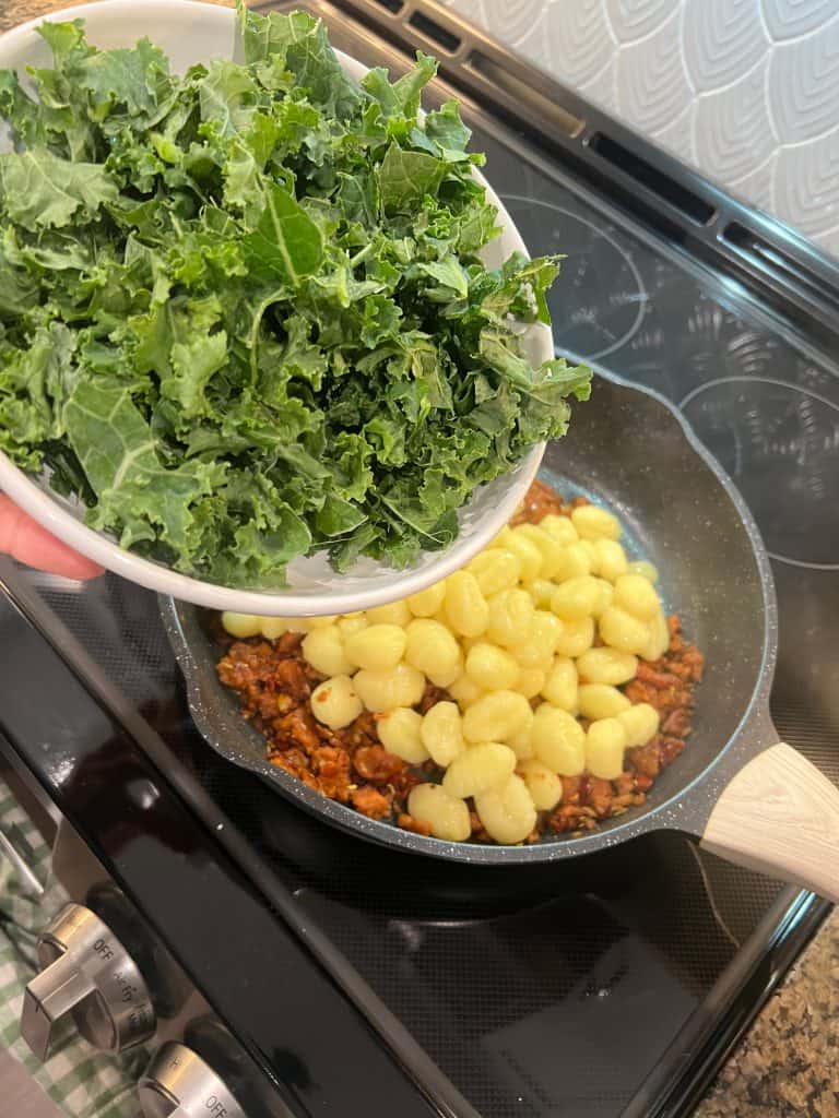 chopped kale going into vegan gnocchi dish