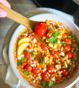 harissa white beans with cherry tomatoes in one pan with lemon slices on spoon